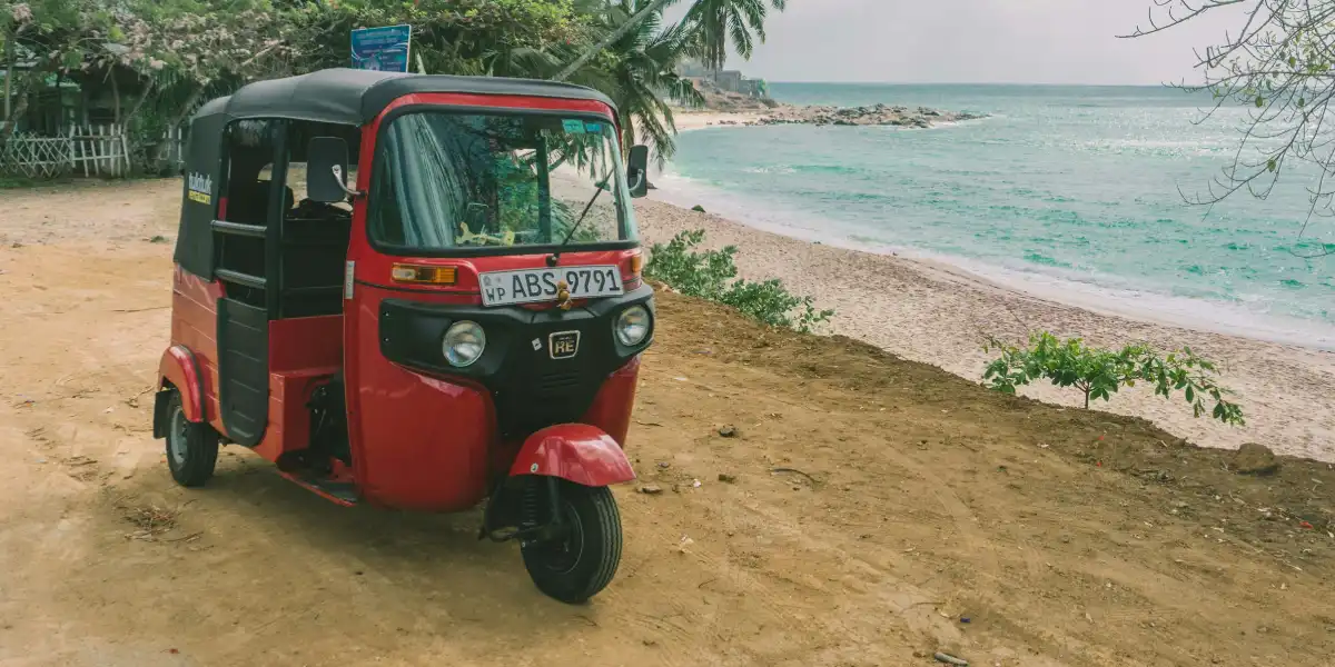 Red tuk-tuk driving along a coastal road in Sri Lanka southern province